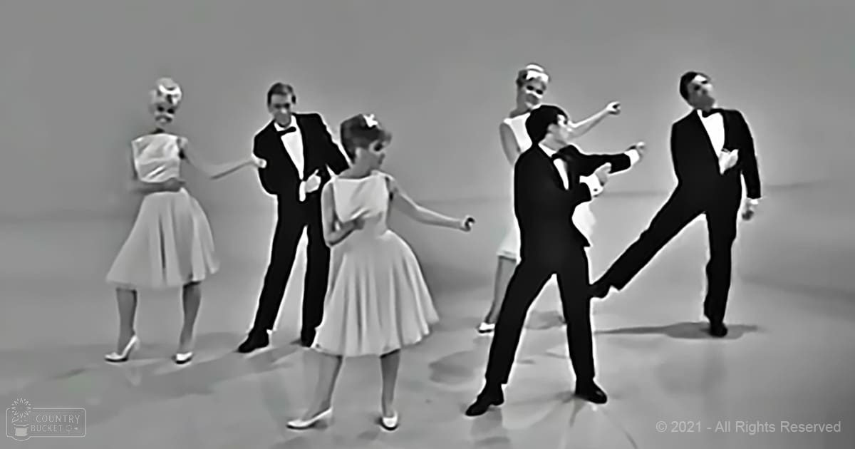 A dance performance scene with multiple individuals in formal attire, set indoors under bright studio lighting.