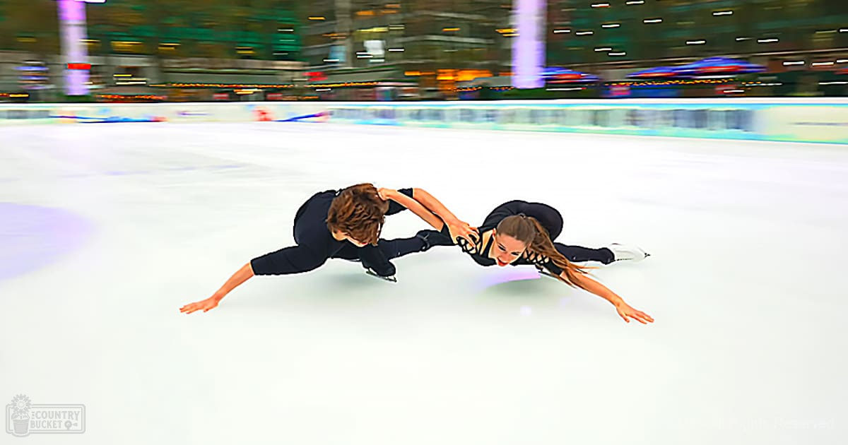 Young adult male and female figure skaters in a well-lit indoor ice rink with smooth skating surface, wearing fitted black attire and white skate boots.