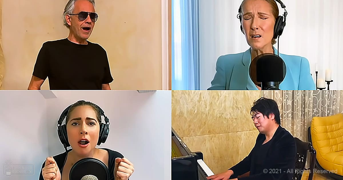 A group singing session in an indoor home or studio setting, with curtains and wall decor visible. Adults are wearing casual attire including t-shirts and blazers.