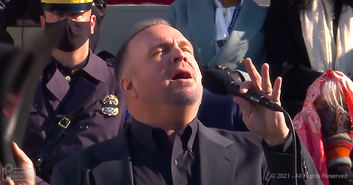Middle-aged man singing at an outdoor event, surrounded by other individuals in a park-like setting with natural light and colorful attire visible.