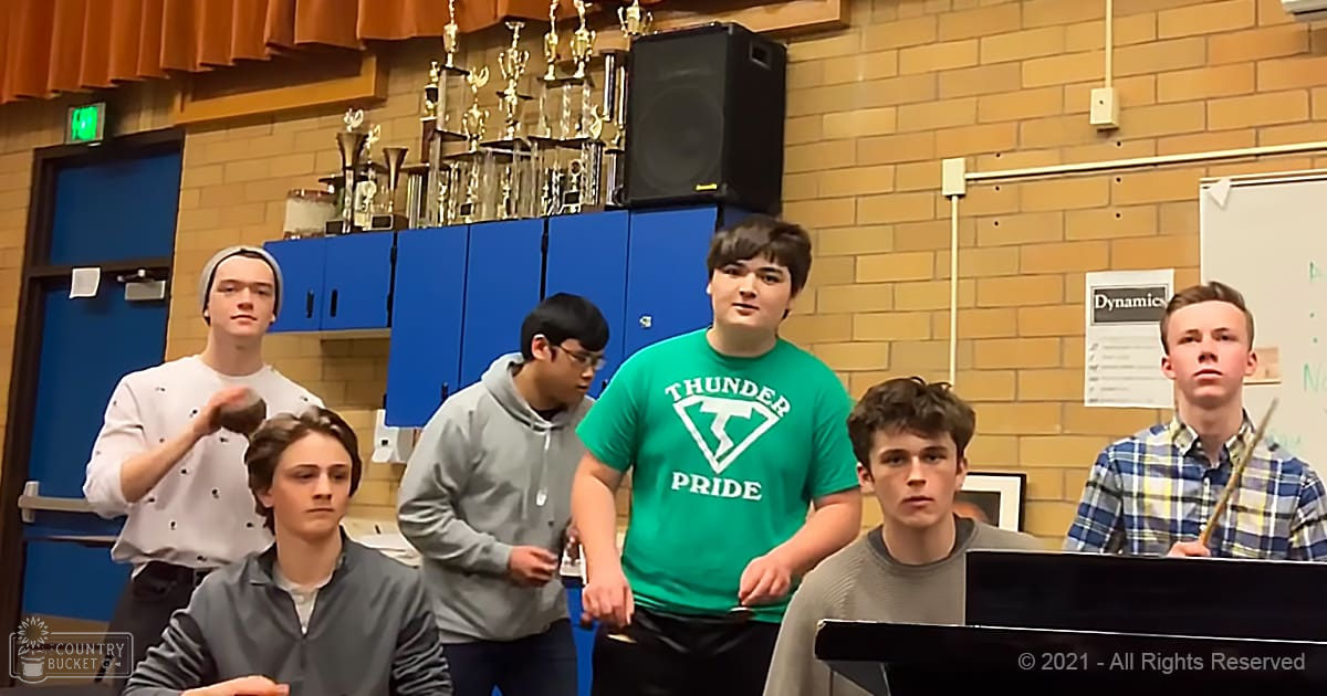 Teenage boys gathered in a school music room, wearing casual shirts with patterns like polka dots and plaid, engaging in a musical activity.