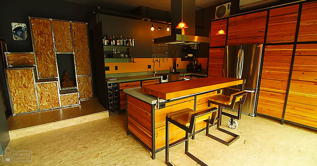 An indoor residential or commercial kitchen space with wooden accents, metal-framed chairs, and pendant lights. The setting suggests evening or night due to the artificial light source used.