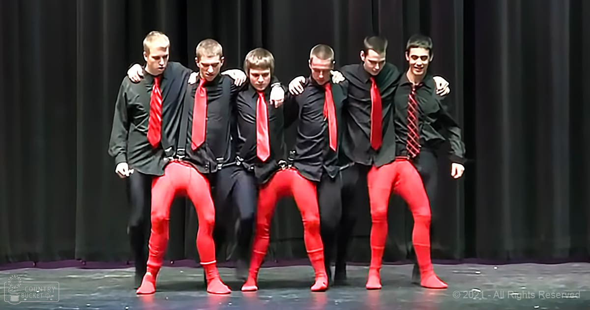 Young adult male singers in a group performance scene on an indoor stage with dark curtains as the background.