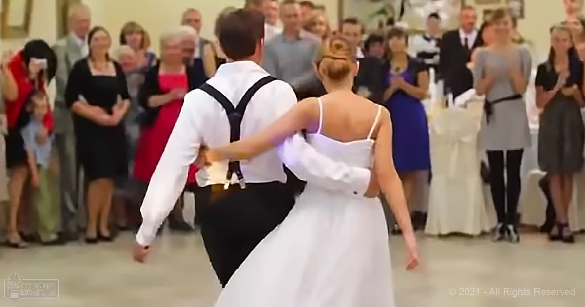 A bride in a white strapless gown dances with her groom at an indoor wedding reception surrounded by guests dressed formally.