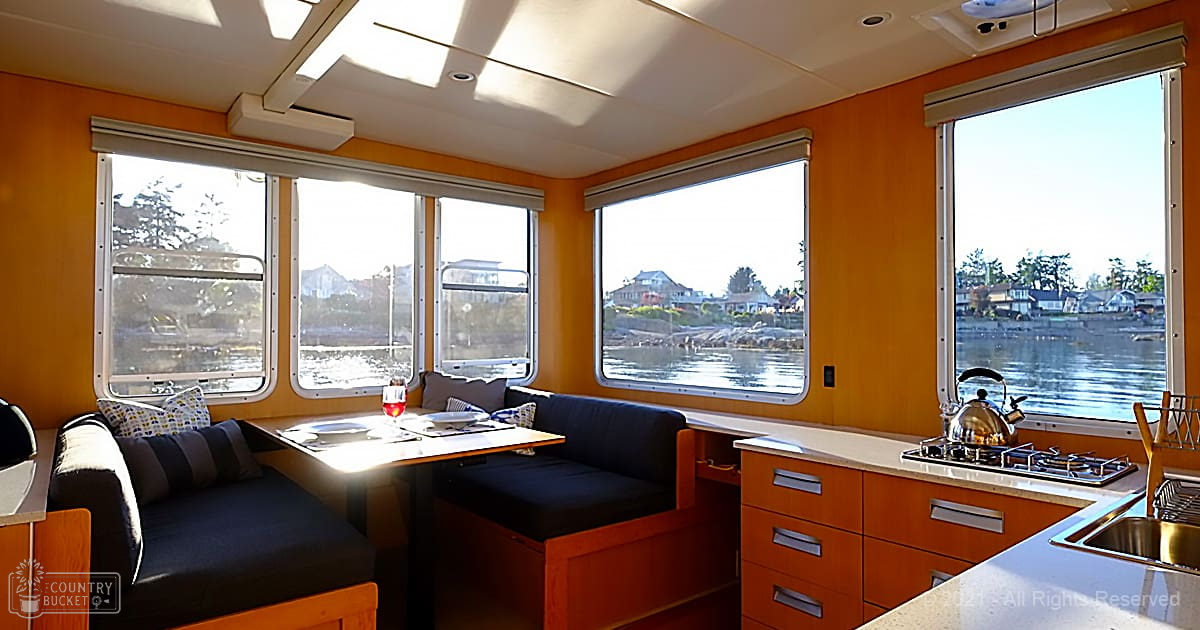 Compact cabin with built-in seating, dining area, kitchen counter, and scenic waterfront view under clear skies.