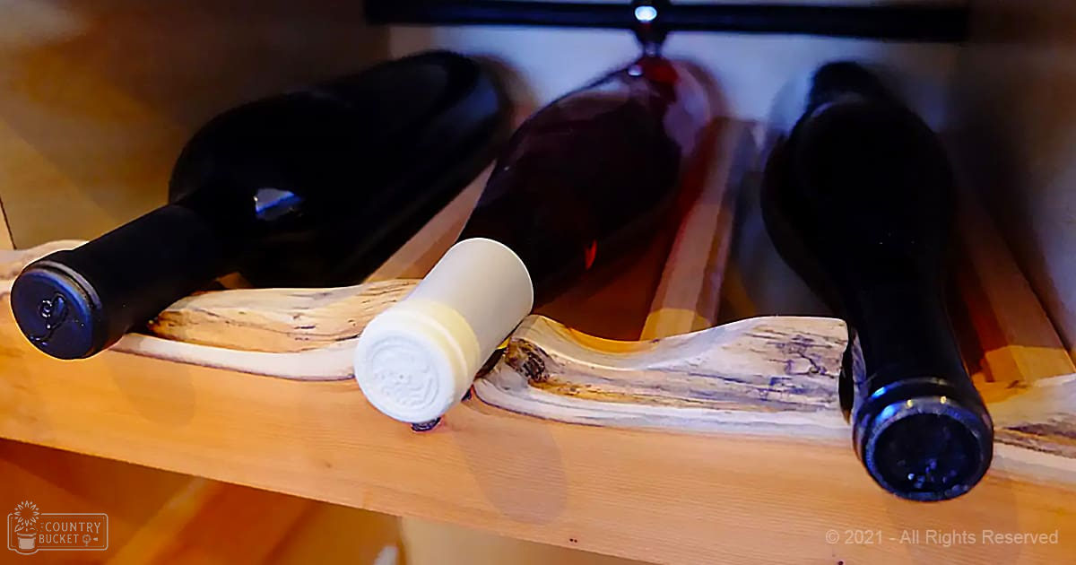 Three dark-colored wine bottles on a wooden wine rack with a white cork, indoors.