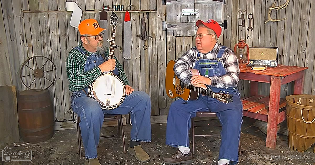 Two older adults playing musical instruments in a rustic old cabin or shed setting.