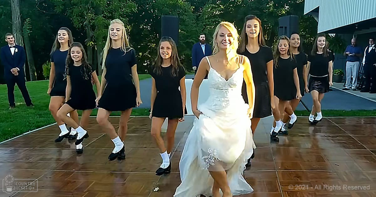 An outdoor wedding reception scene with a bride in a white wedding dress and young adults wearing black dresses, surrounded by greenery and natural light.