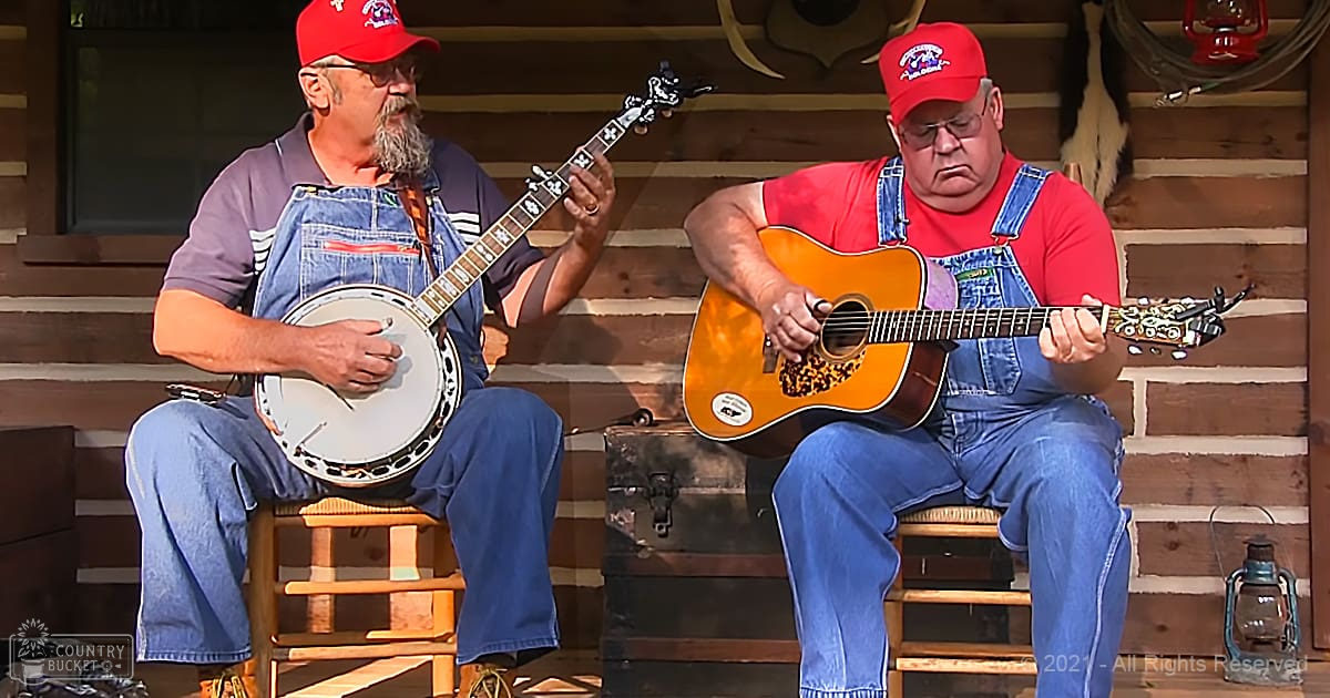Two musicians playing banjo and guitar in a rustic outdoor setting with lanterns and wooden walls.