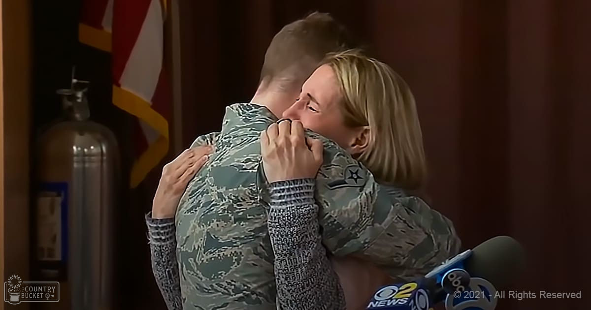 A heartfelt reunion between a soldier wearing a modern U.S. Air Force camouflage uniform and a woman in a loose gray sweater, set against an indoor backdrop with microphones from 'abc 2 NEWS' and the U.S. Air Force flag visible.