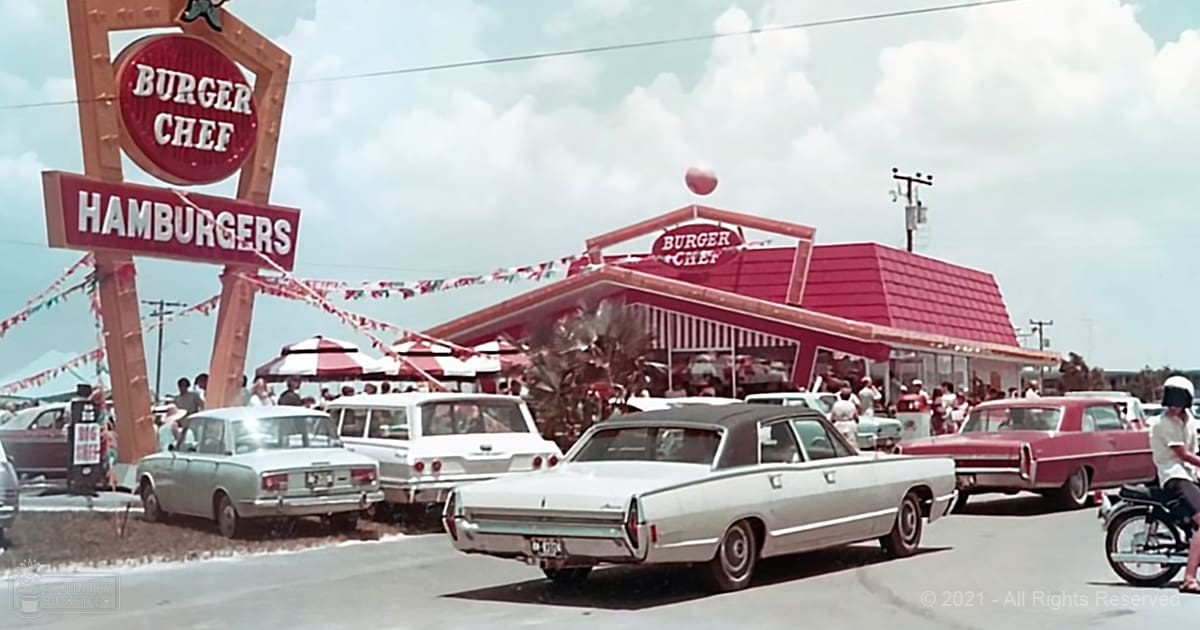 An outdoor Burger Chef restaurant with several people near the entrance and a motorcycle rider in the foreground, under a clear sky with palm trees suggesting summer.