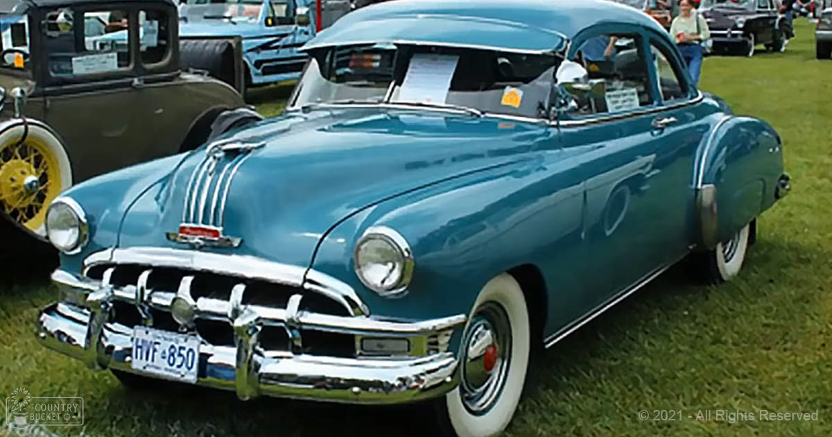A classic teal-colored car with chrome details at an outdoor car show on a grassy field under natural daylight.