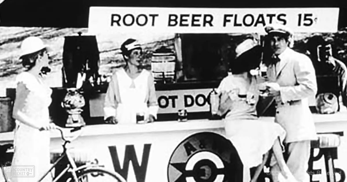Vintage root beer float stand at a summer fairground with people in period attire and a bicycle in the foreground.