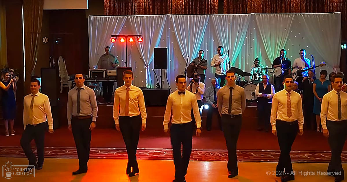 Young adults performing at an indoor wedding reception with formal attire, red stage lights, and various shades of beige, yellow, black, and blue from clothing and curtains.
