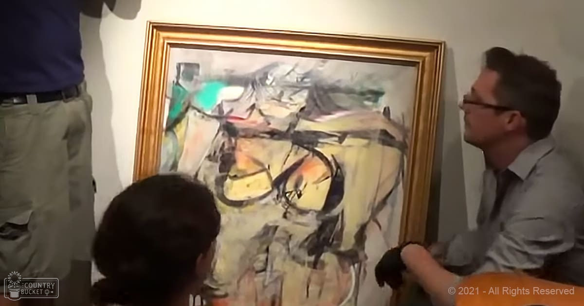 A group of individuals examining an abstract painting in a museum or art gallery setting, with artificial lighting and light-colored walls.