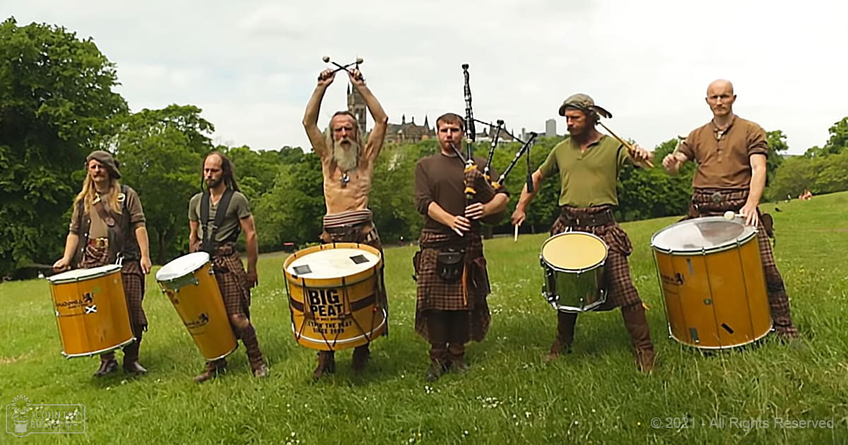 Adult males performing traditional Scottish music in an open park with greenery, spring or summer setting, natural daylight.