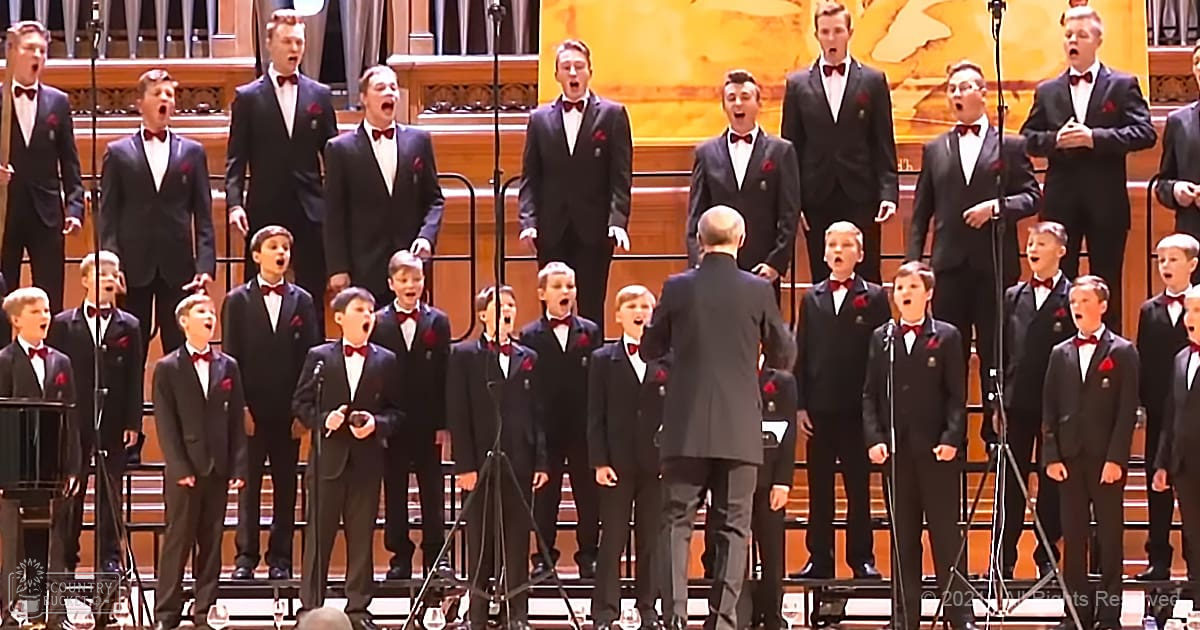 Adults performing on stage with microphones, sheet music stands, conductor, ornate stage setup, warm indoor lighting.