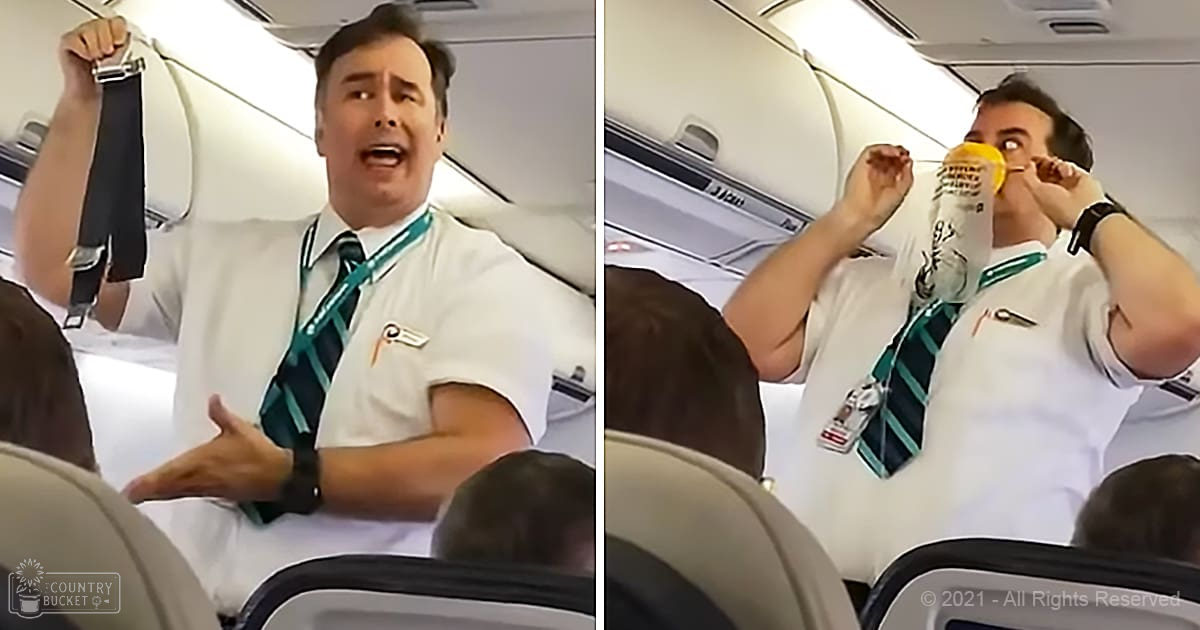 An adult male flight attendant in an airplane cabin demonstrating safety procedures, with a seated passenger partially visible in the background.
