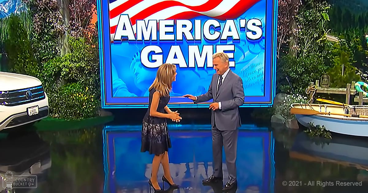 A game show set with a backdrop with 'AMERICA'S GAME' in bold white letters against a blue background. Decorative elements like plants and water features are visible, suggesting an indoor studio setting.