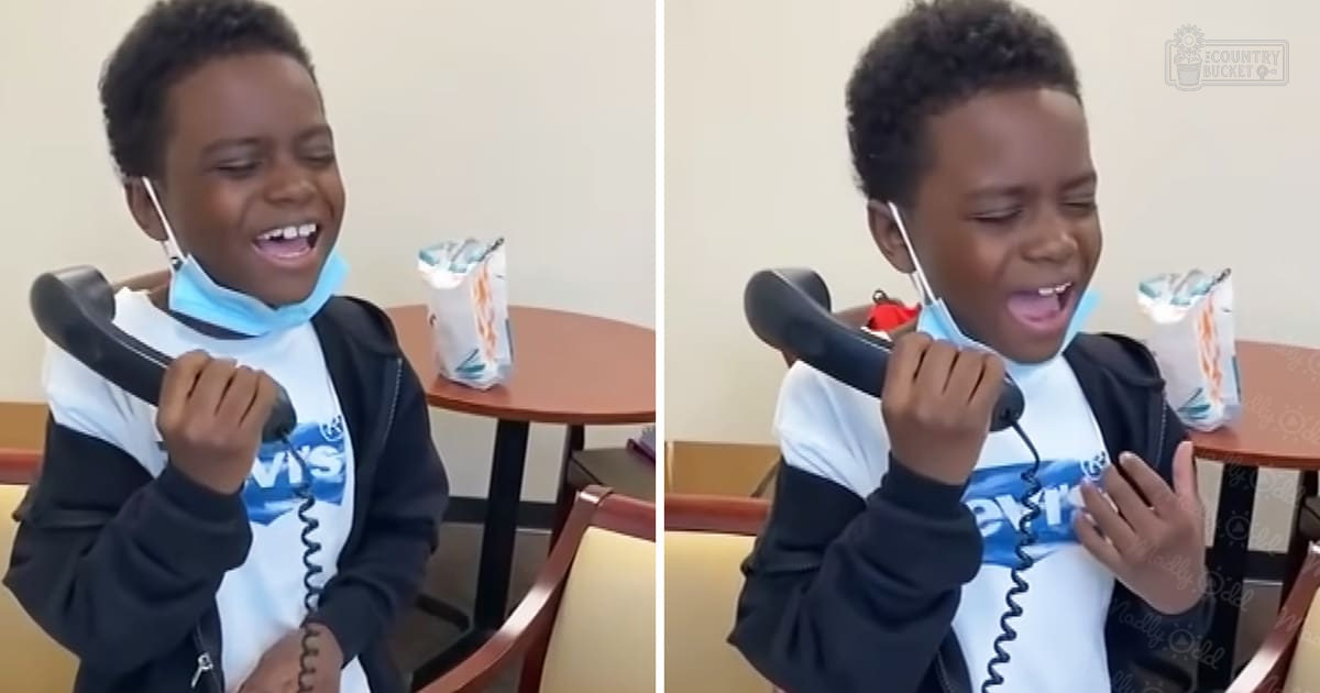 A child in a fast-food restaurant, wearing a white t-shirt with 'Levi's' logo and black zip-up hoodie, holding a black telephone handset.
