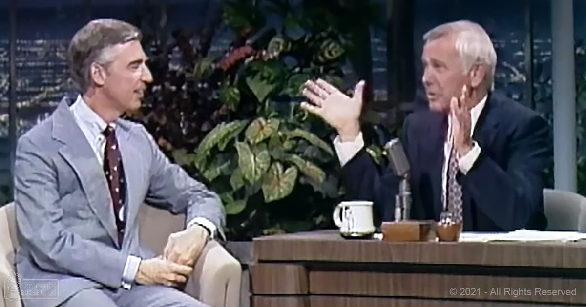 Talk show setting with two adult males in formal attire against an urban backdrop and indoor lighting.