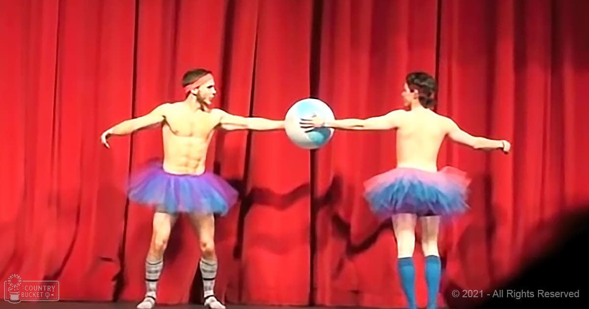 Two individuals in tutus performing at a school play or community theater production, holding a beach ball against a red curtain backdrop with artificial lighting.