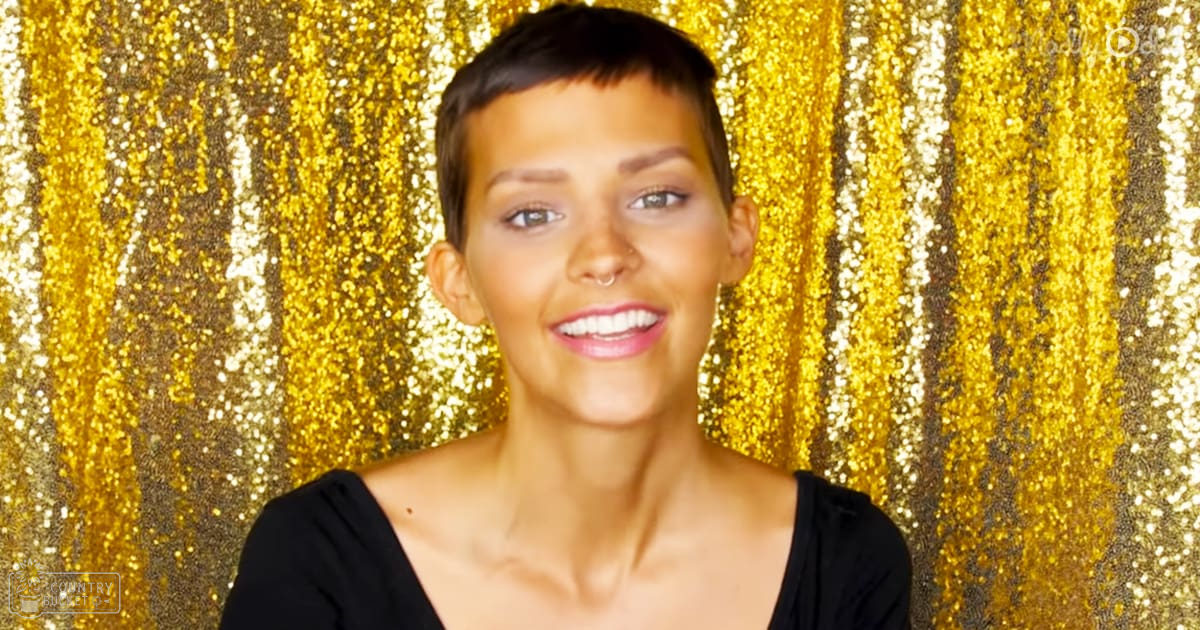 A young adult female wearing a black top with a low neckline and short sleeves, standing against a festive gold glittery curtain backdrop.