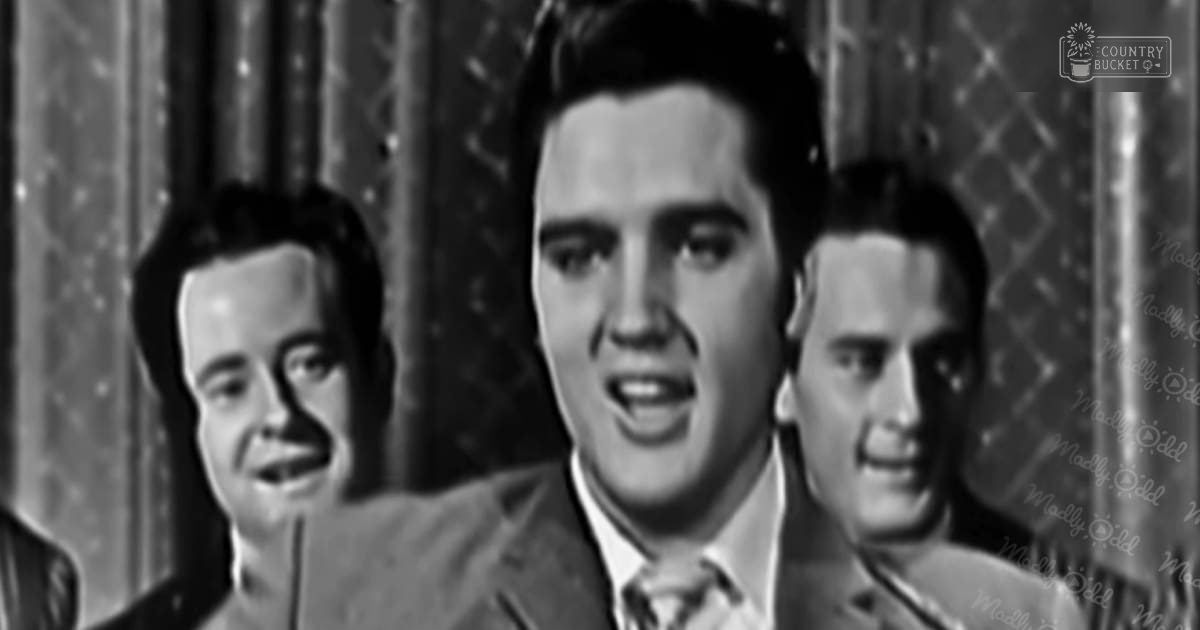A young adult male in a mid-20th century suit indoors with patterned curtains suggesting an indoor stage or studio setup, black and white image.