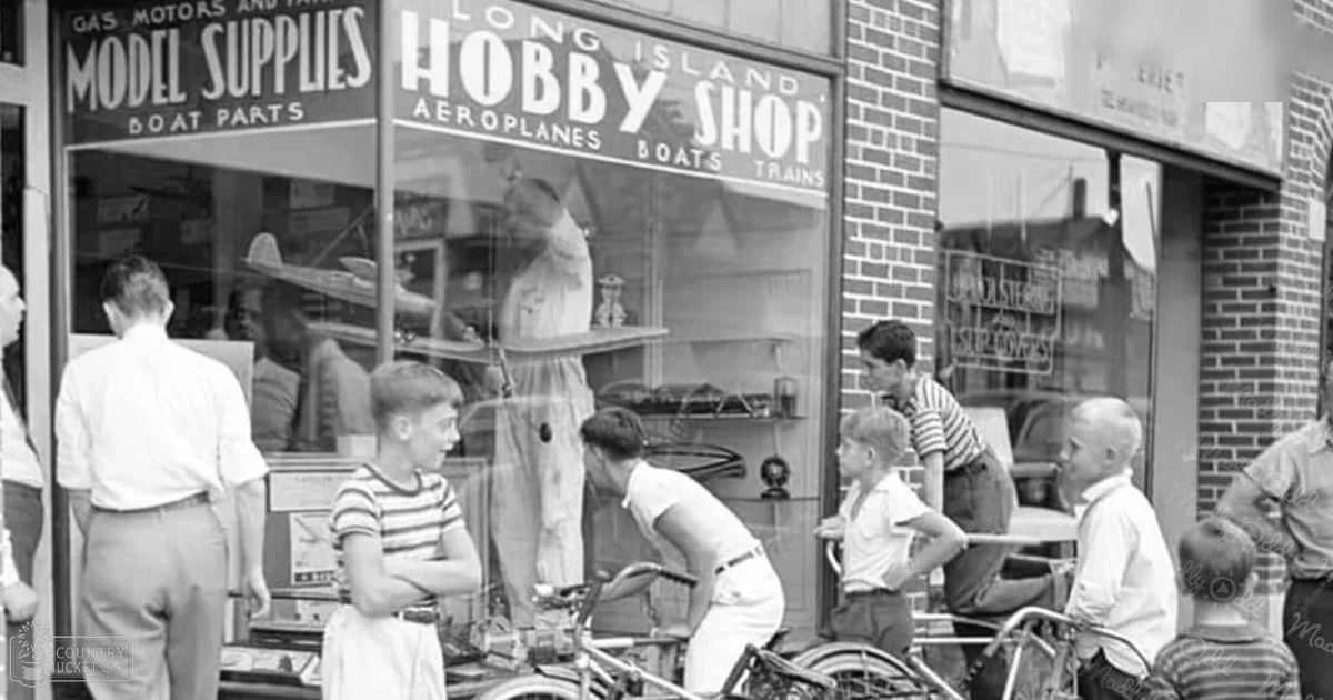 Group of children wearing striped shirts and light-colored pants standing in front of a hobby shop with bicycles visible, Long Island, New York.