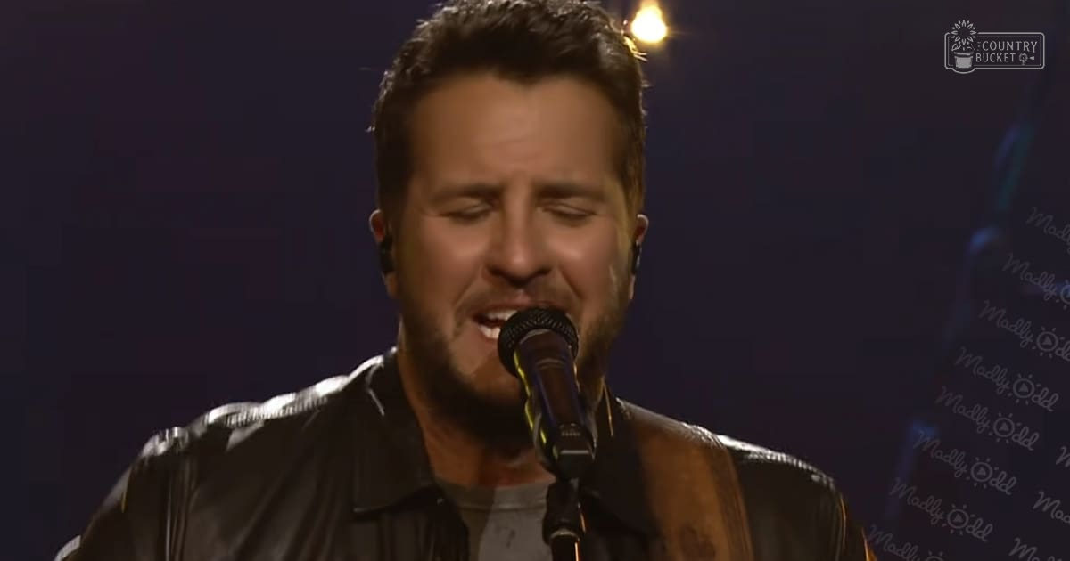 A male adult singer wearing a relaxed-fit, black leather jacket with long sleeves on stage under dim lighting.