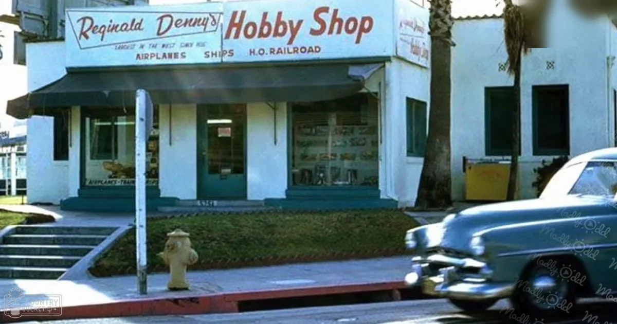 Urban street scene with Reginald Denny's Hobby Shop, vintage car, fire hydrant, palm trees, and warm daylight.