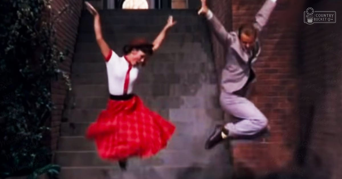 A dance scene from 'West Side Story' in an urban alleyway with brick walls and steps, with a female dancer wearing a red skirt and white top, and a male dancer in a light-colored suit.