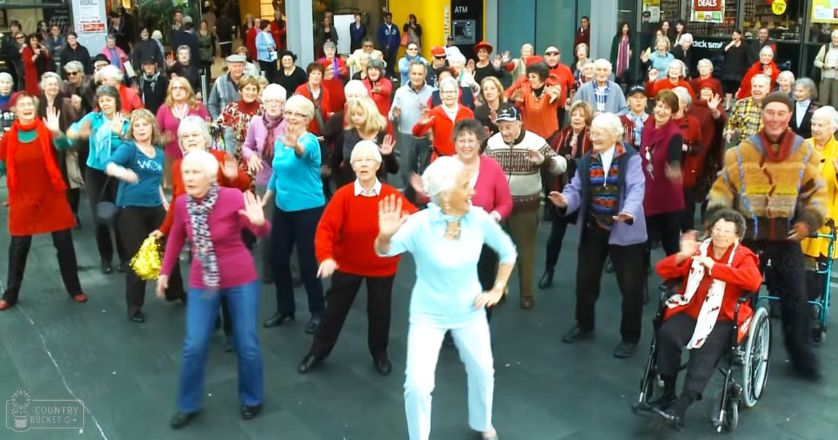 A group of middle-aged to older adults performing a dance in an urban public space during the day.