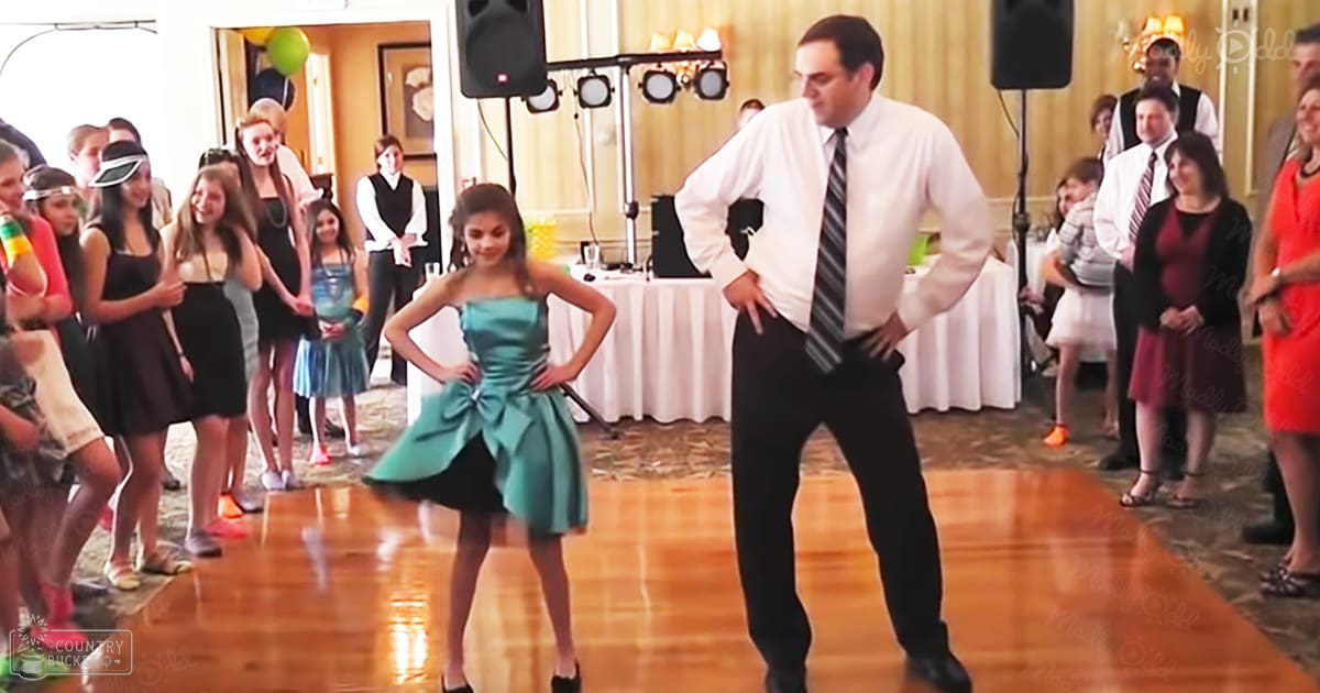 A young girl dancing with an adult man at what appears to be a wedding reception, surrounded by guests and festive decorations.