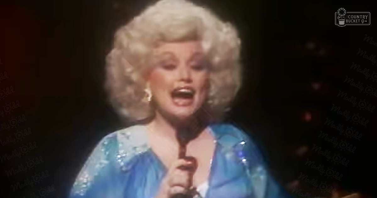 Adult female performer in a formal, sequined blue gown with long sleeves and large hoop earrings on stage under spotlighting.