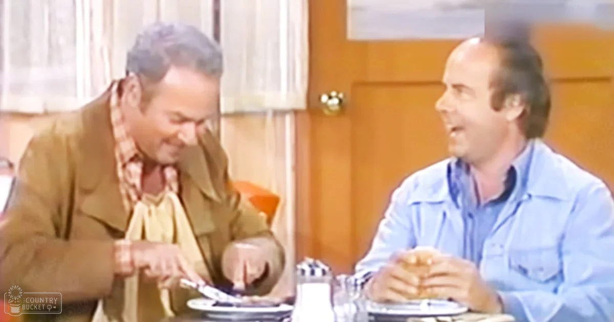 Two middle-aged men dining in a casual indoor setting with natural light filtering through sheer curtains, suggesting daytime in spring or summer.