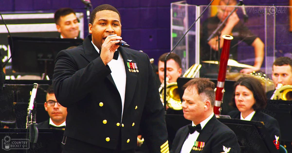A male singer performing on stage with an orchestra at a formal indoor event.