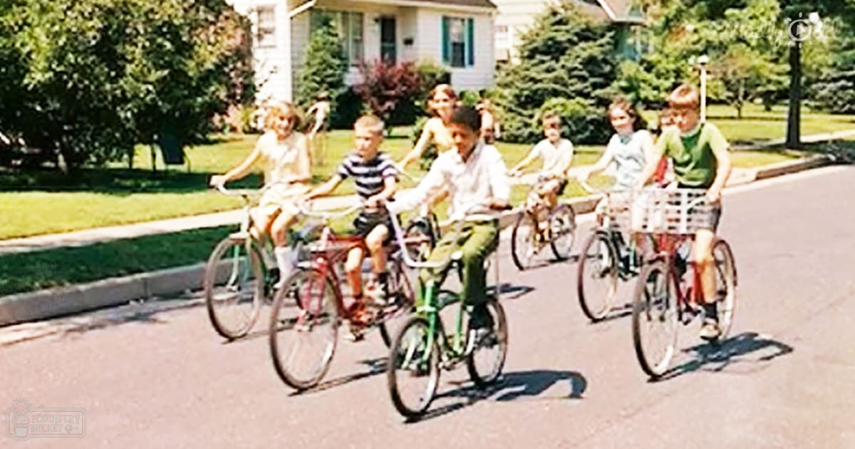 Children riding bicycles in a suburban neighborhood with greenery and summer attire.