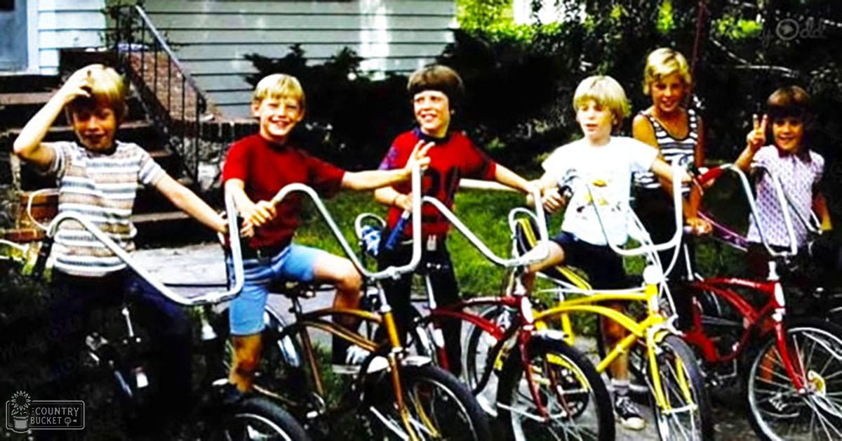 Young children with bicycles in a suburban summer scene by a house.