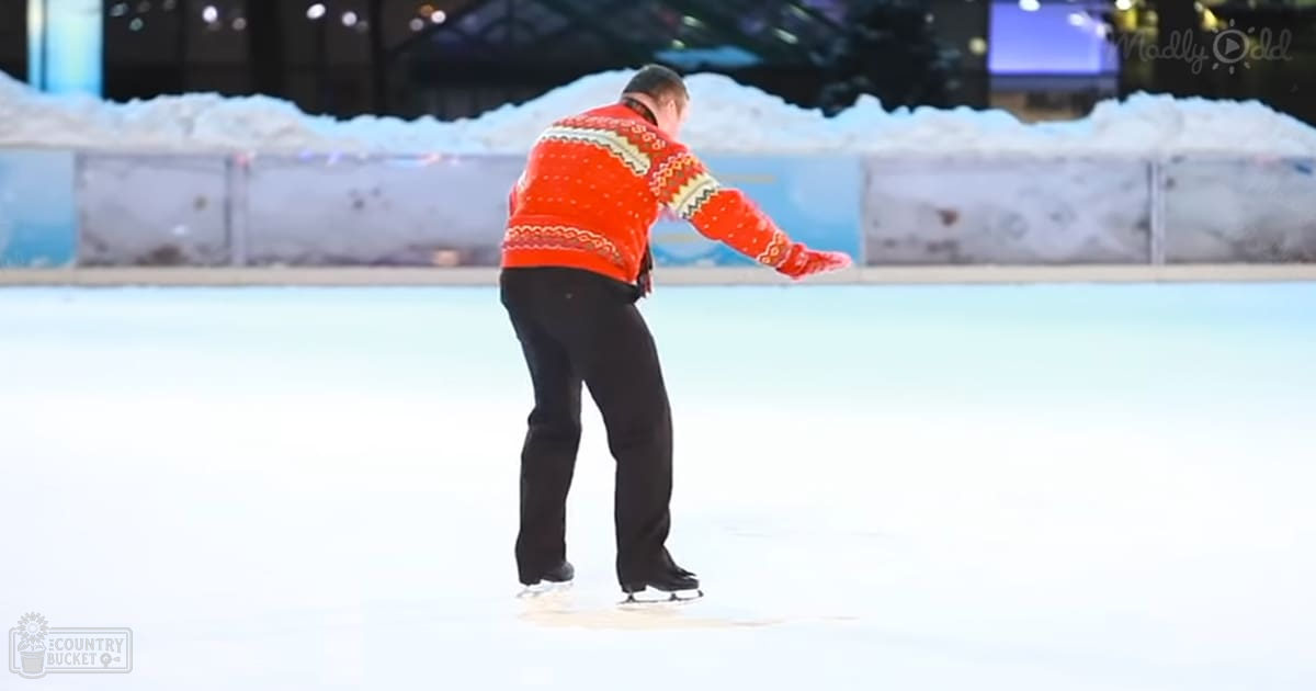 A middle-aged adult male skating in an indoor ice rink, wearing a red sweater with white and yellow geometric patterns on a wool blend fabric.