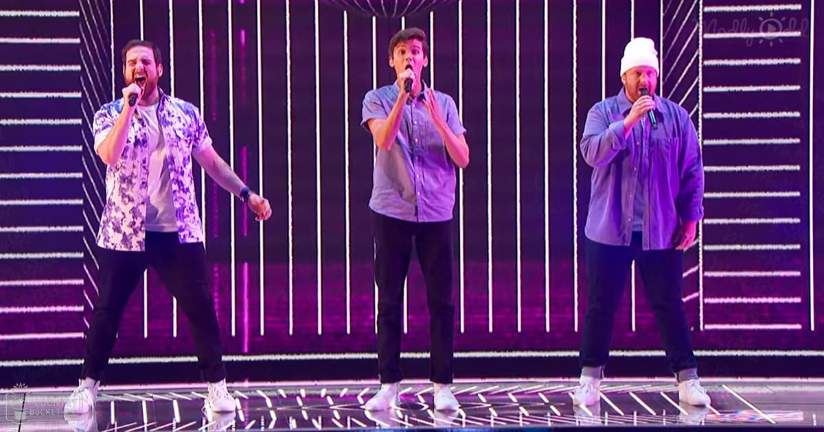 A musical performance scene with young adult males wearing patterned shirts and sneakers, set against a modern stage backdrop with vibrant lighting during the evening.
