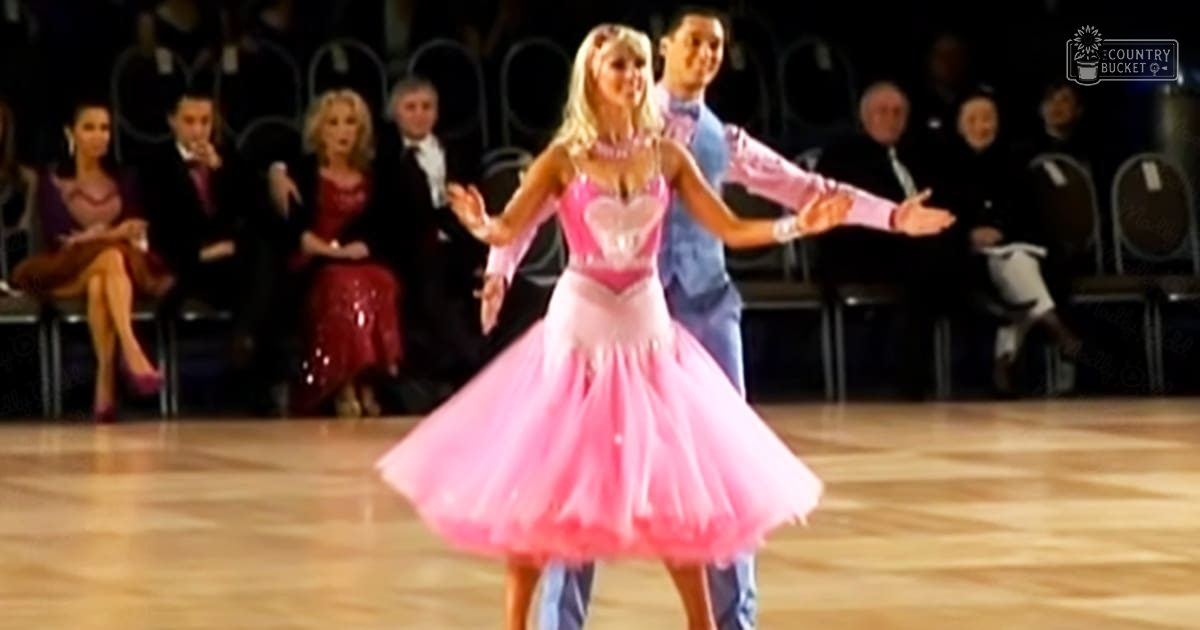 A young adult female dancer performing in a formal indoor ballroom setting, surrounded by an audience dressed for a dance event.