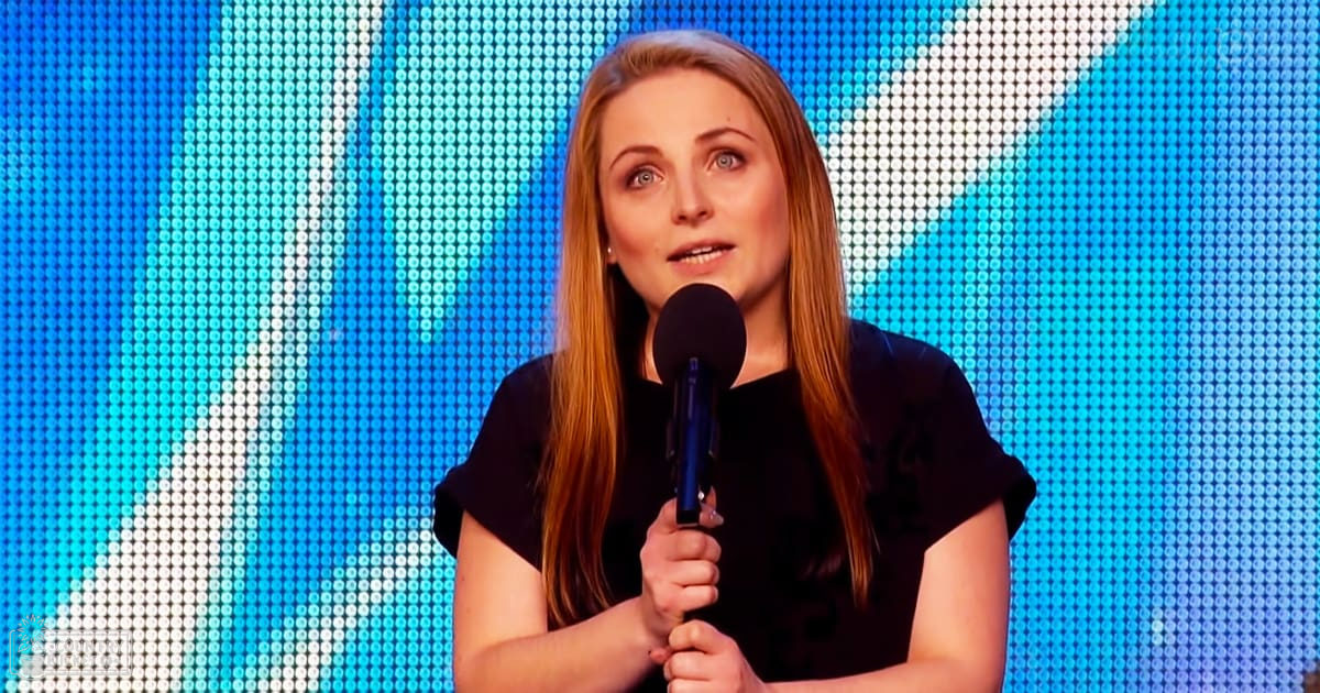 A young adult female in a relaxed, modern casual black top holding a microphone against a bright blue and white LED screen backdrop.