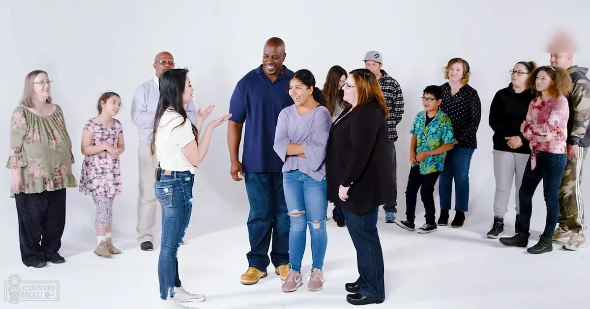 Group photograph taken indoors with children and adults dressed in casual attire against a plain white backdrop, under bright artificial light.