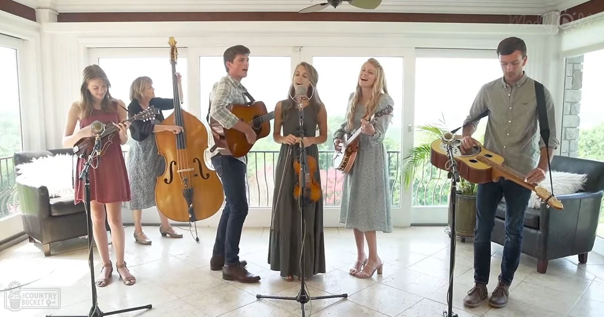A small ensemble performing music indoors, possibly in a home setting with natural light from large windows.