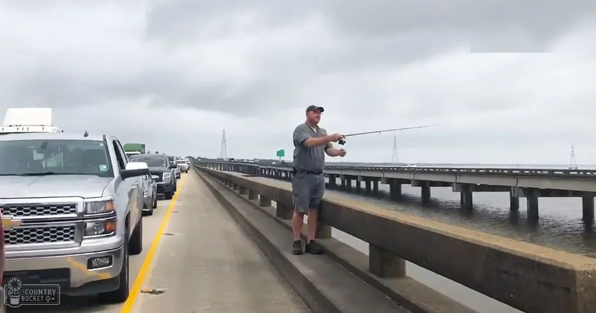 An adult male fishing from a highway overpass under an overcast sky.