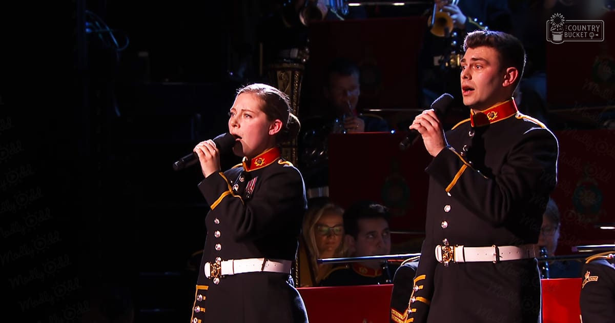 Young adult male and female singers in uniform performing on a dimly lit indoor concert stage with red and gold accents.