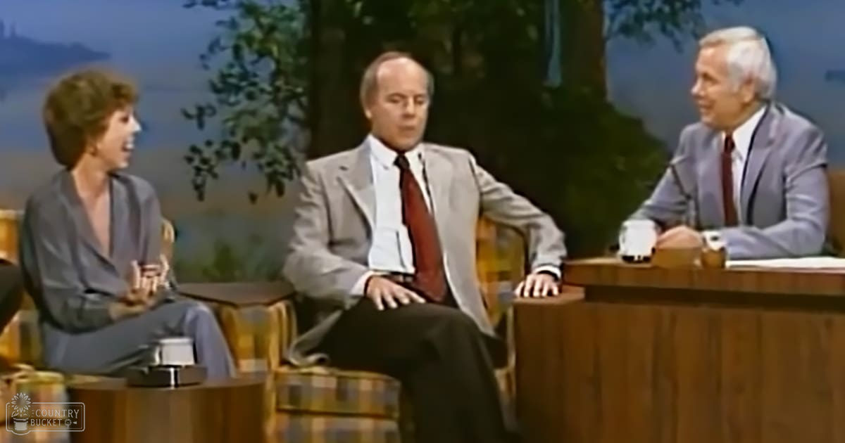 A talk show set from the 1970s with three adults seated, dressed formally, against a backdrop of trees and mountains under natural daylight.