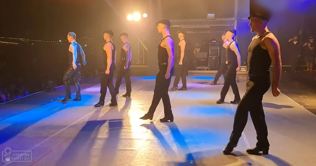 Young adult male dancers in a dance performance on a stage with artificial lighting at evening time.