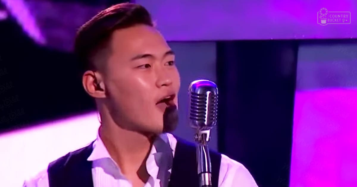 A young adult male singer in formal attire performs into a vintage microphone on stage under focused lighting.